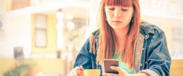 Photo of a serious young woman drinking coffee and staring at her phone.