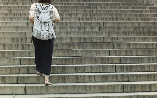 Photo of a woman in a skirt, wearing a backpack and walking away from the camera up a flight of concrete stairs