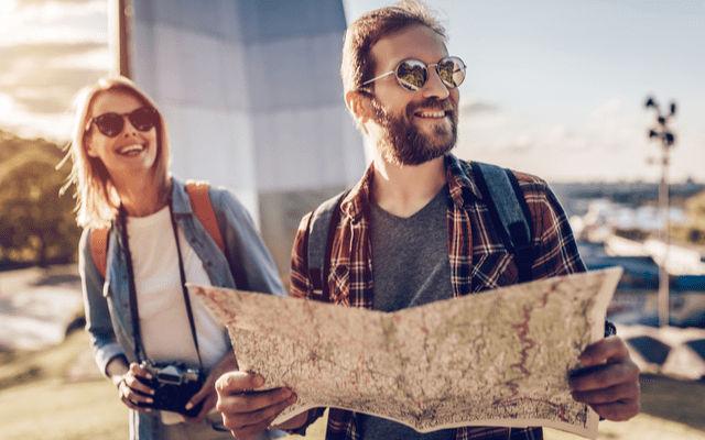 Photo of two tourists wearing sunglasses and smiling while holding a map