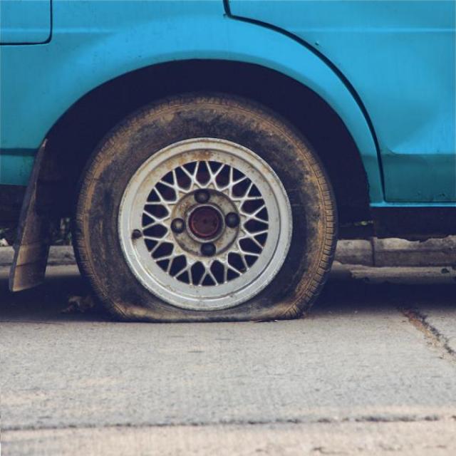 Front of a teal car with one tire very flat.